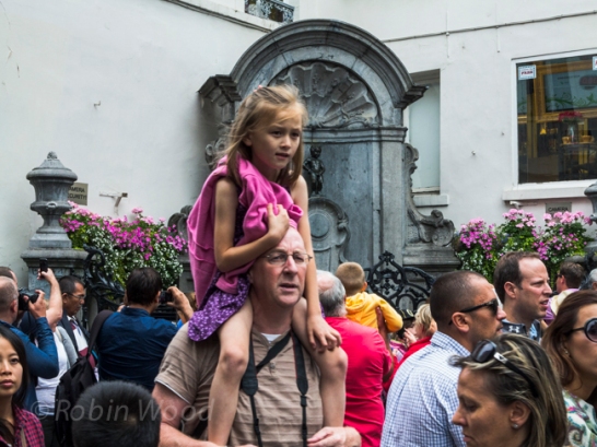 A small girl gets a shoulder ride past the small statue Manneken Pis.